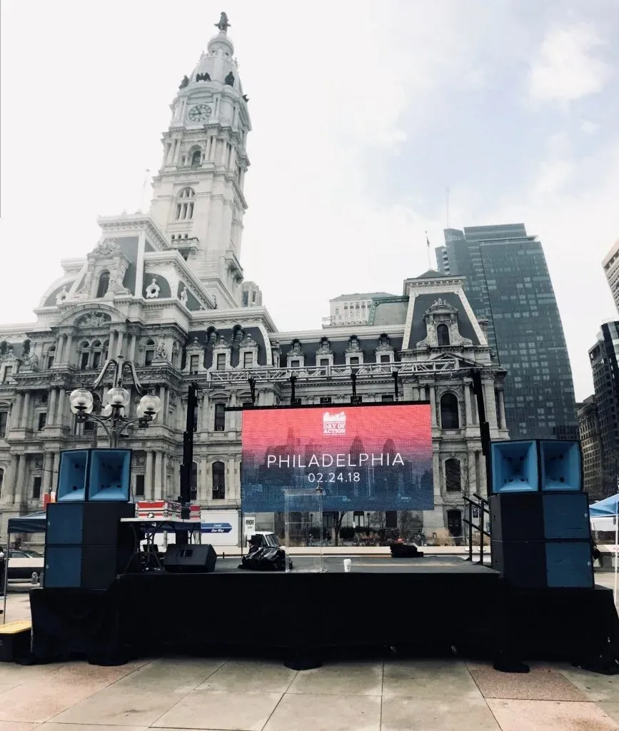 An outdoor stage in front of Philadelphia City Hall with a large LED video wall and flanking loudspeaker arrays.